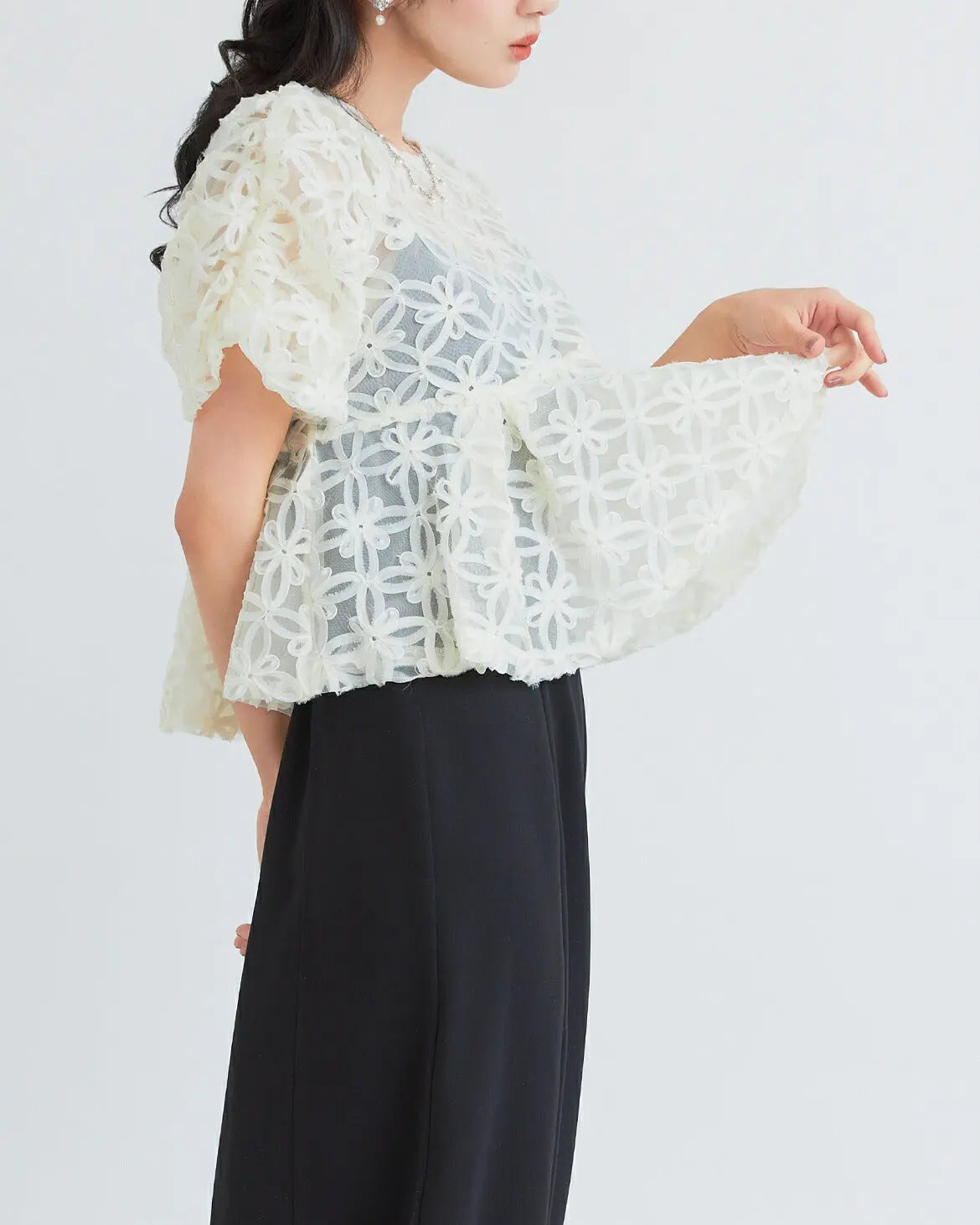 モデル着用:立体的な刺繍生地を使用したトップスとペプラムデザインのウエスト切り替え 上半身アップ ペプラムデザイン詳細 ベージュxブラック